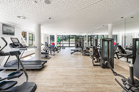 Moderner Fitnessraum mit Trainingsgeräten und viel Tageslicht.