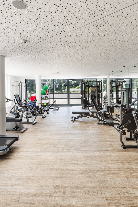 Moderner Fitnessraum mit Trainingsgeräten und viel Tageslicht.
