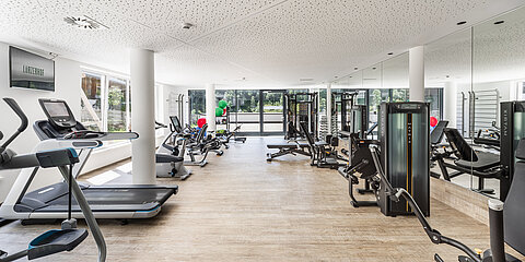 Moderner Fitnessraum mit Trainingsgeräten und viel Tageslicht.