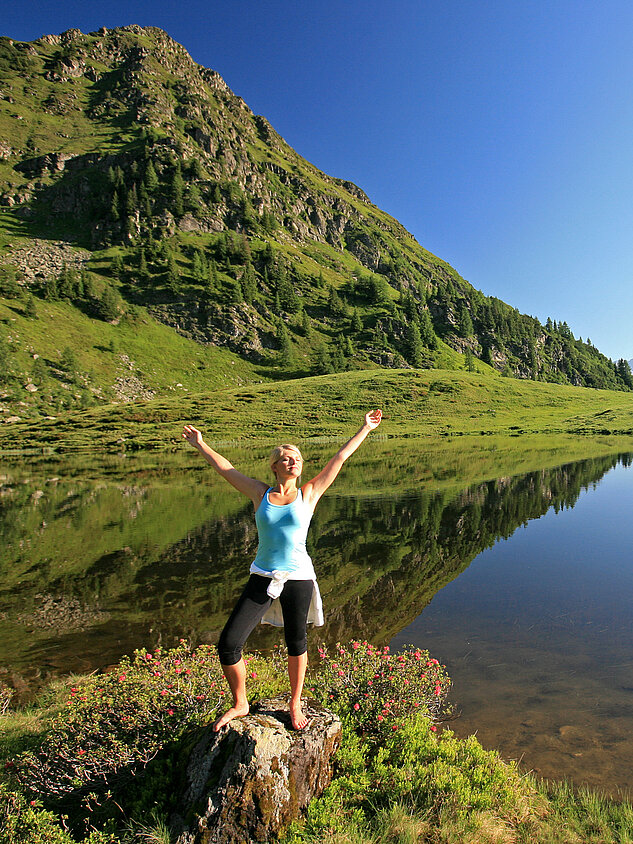 Eine Frau genießt die Natur an einem Bergsee während ihres Aktivurlaubs in Österreich