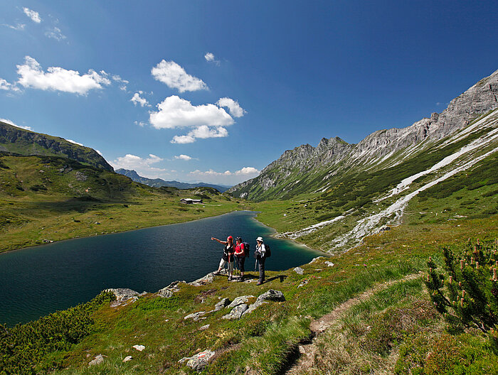 Drei Wanderer genießen die Aussicht auf einen Bergsee beim Aktivurlaub in Österreich.