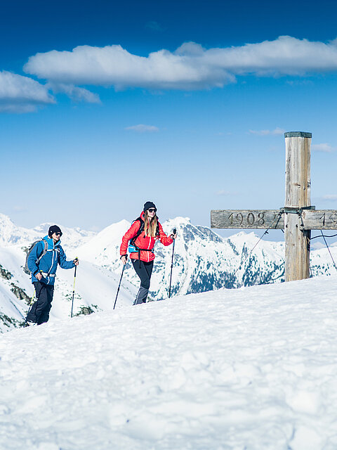 Zwei Skitourengeher am Gipfelkreuz mit Panoramablick auf verschneite Alpen in Obertauern