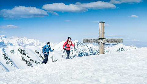 Zwei Skitourengeher am Gipfelkreuz mit Panoramablick auf verschneite Alpen in Obertauern