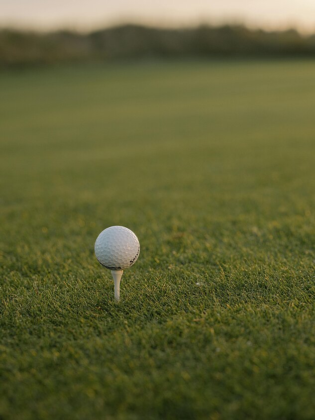 Golfball auf Tee auf gepflegtem Grün bei Sonnenuntergang