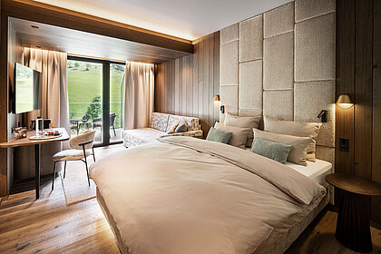 Modernes Doppelzimmer im Lürzerhof nahe Obertauern mit gemütlicher Sitzecke, Balkon und Blick auf die grüne Berglandschaft