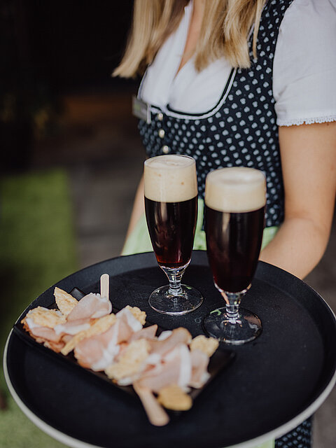 Eine Servicekraft mit einem Tablett auf dem ein leckerer Snack und zwei Getränke sind, im Gourmet & Wellnesshotel Lürzerhof