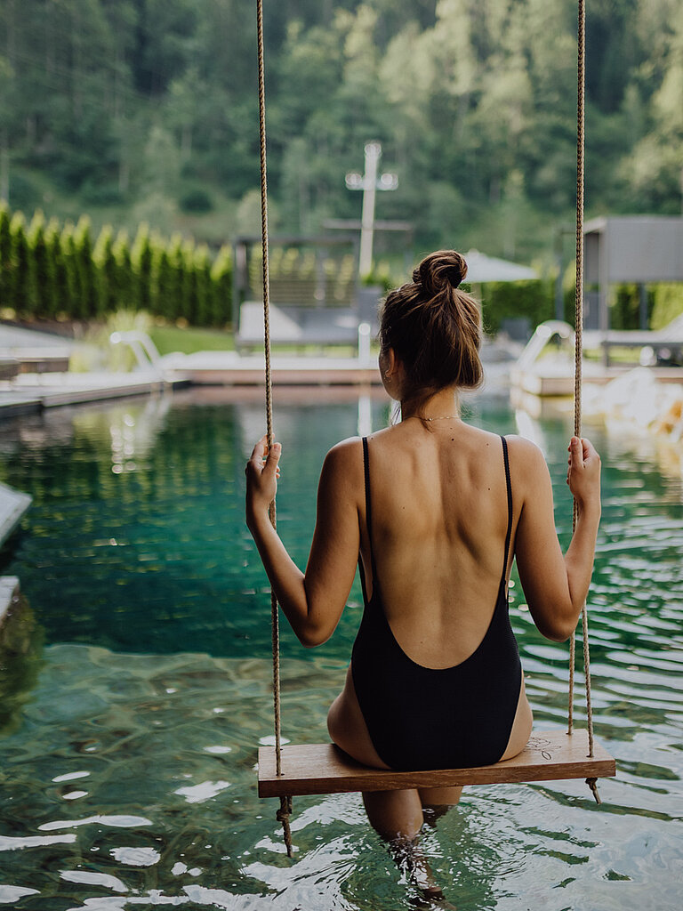 Eine Frau schwingt auf einer Schaukel über dem Naturpool im Wellnesshotel Lürzerhof in Salzburg.