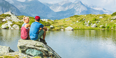 Zwei Wanderer sitzen auf Felsen am Bergsee in Obertauern