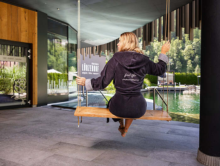 Frau im Bademantel auf einer Schaukel im Spa-Bereich mit Naturblick.