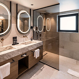 Modernes Badezimmer einer Suite im Wellnesshotel Lürzerhof nahe Obertauern mit Doppelwaschtisch und großzügiger Walk-in-Dusche
