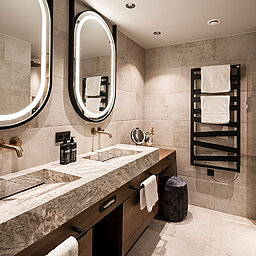 Modernes Badezimmer im Lürzerhof nahe Obertauern mit Doppelwaschtisch aus Naturstein, beleuchteten Spiegeln und elegantem Spa-Design