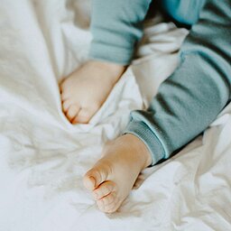 Babyfüße auf weißer Decke in gemütlicher Schlafkleidung