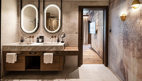 Edles Badezimmer im Lürzerhof bei Obertauern mit Doppelwaschtisch, beleuchteten Spiegeln und hochwertigem Naturstein-Design