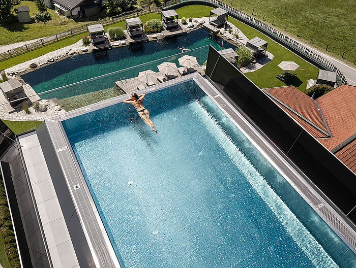 Infinity Sky Pool des Wellnesshotels Lürzerhof aus der Vogelperspektive mit Naturbadeteich und Liegebereichen im Hintergrund