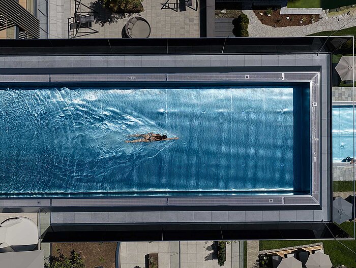 Schwimmerin im großzügigen Infinity Sky Pool des Wellnesshotels Lürzerhof nahe Obertauern aus der Vogelperspektive