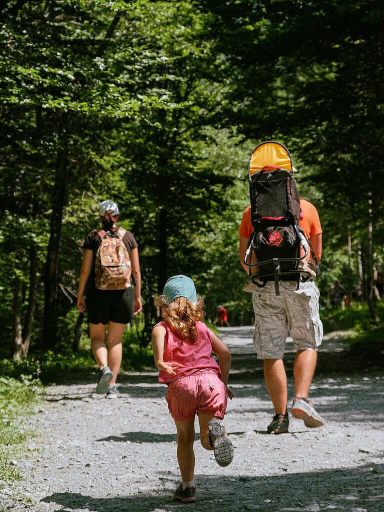 Family hiking through a shady forest path with a toddler