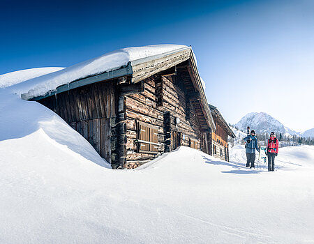Zwei Skitourengeher vor verschneiter Berghütte bei strahlendem Winterwetter in Obertauern