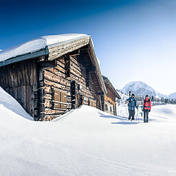 Zwei Skitourengeher vor verschneiter Berghütte bei strahlendem Winterwetter in Obertauern