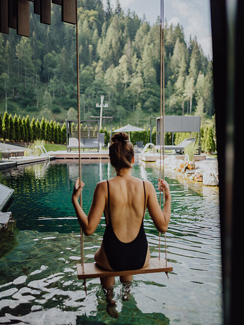 Eine Frau schwingt auf einer Schaukel über dem Naturpool im Wellnesshotel Lürzerhof in Salzburg.