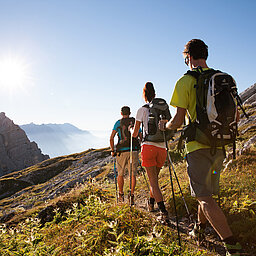 Wandergruppe mit Trekkingstöcken auf Bergpfad bei Sonnenschein
